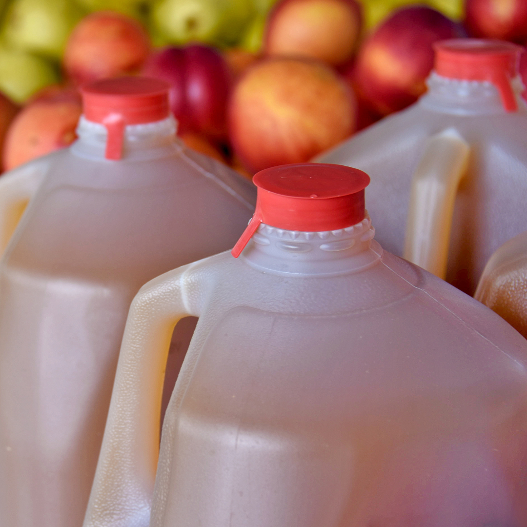 three plastic gallons of apple cider in front of red and green apples